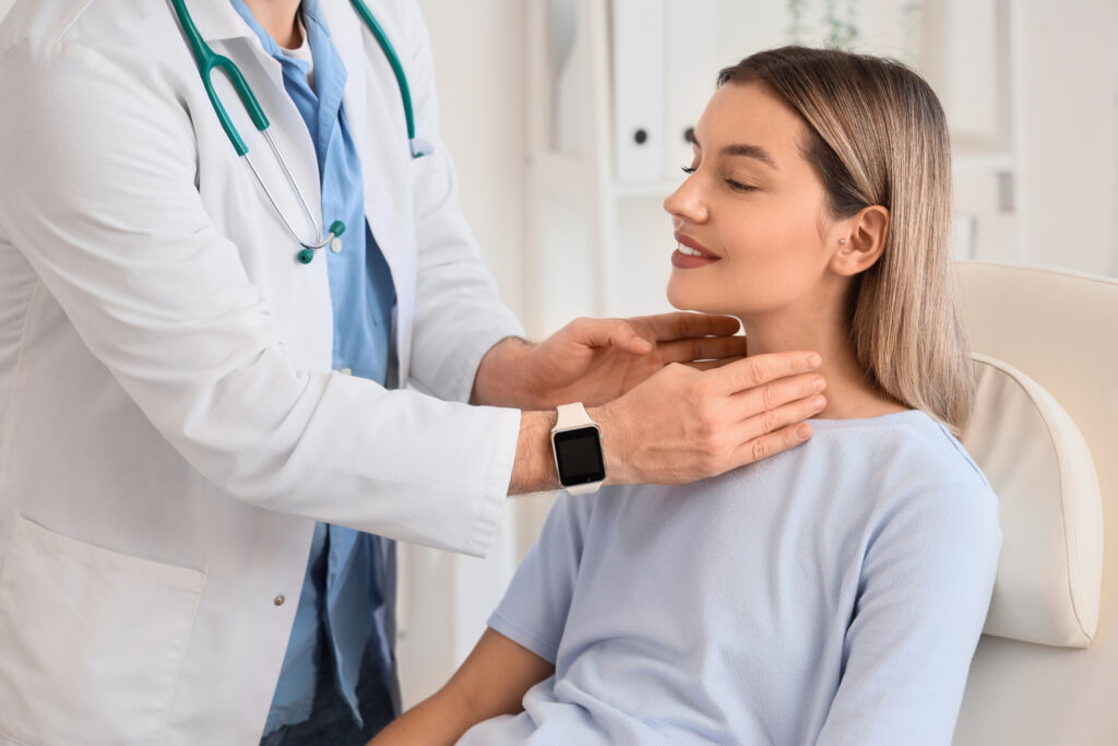 Male endocrinologist examining thyroid gland of young woman in clinic